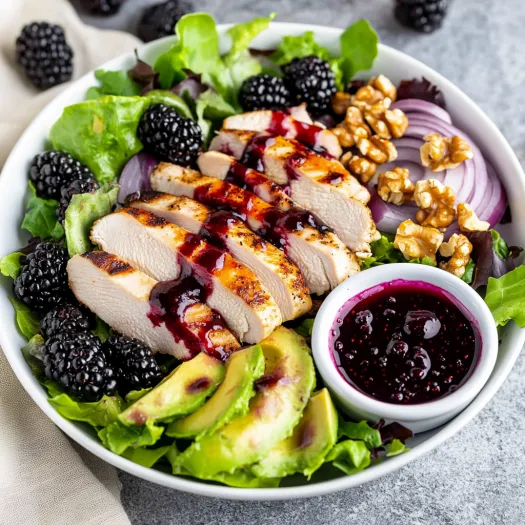 A plate of food with chicken, avocado, and blackberries.