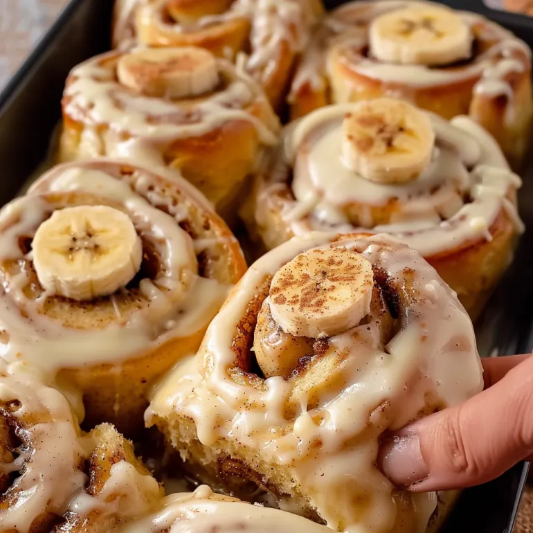 A person is holding a cinnamon roll with bananas on top.