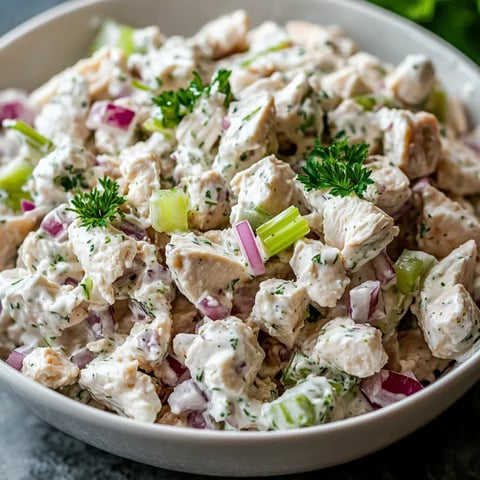 A bowl of chicken salad with onions and parsley.